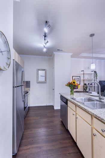A kitchen with a refrigerator, sink, and wooden floors.